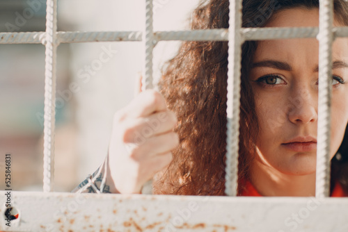 Young brunette curly woman in orange suit behind jail bars. Female in colorful overalls portrait photo