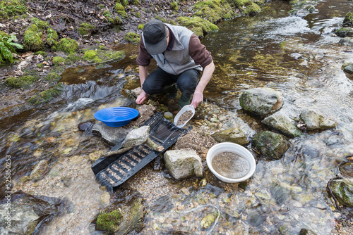 Outdoor adventures on river. Gold panning, man pours sand and gravel into a sluice box in search of gold in a small mountain stream photo