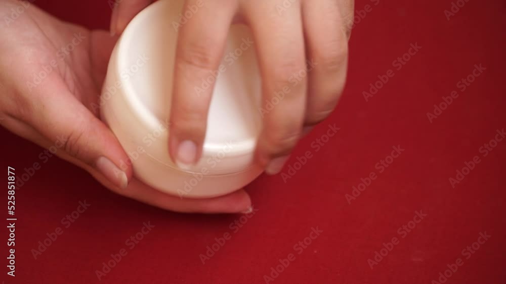 Women's hands unscrew a white jar of cream. Women's hands unscrew a white jar of cream.