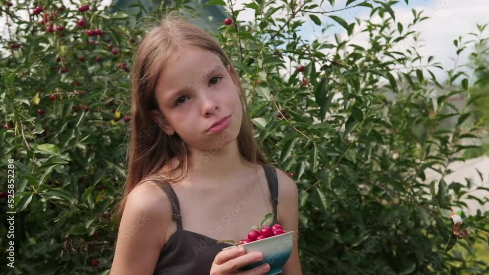 An offended, upset teenage girl is crying in the garden against the background of a cherry tree on a summer day, holding a bowl of cherries in her hands An offended, upset teenage girl is crying in the garden against the background of a cherry tree on a summer day, holding a bowl of cherries in her hands