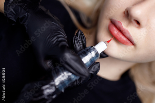 Фотография Cosmetologist master apply red permanent lips tattoo on young woman