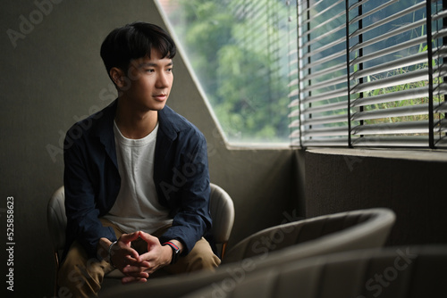 Canvas Print A handsome Asian man in a casual shirt is contemplating and looking out the window