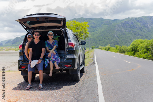 Portrait of three people sitting on back of a truck in countryside road trip.