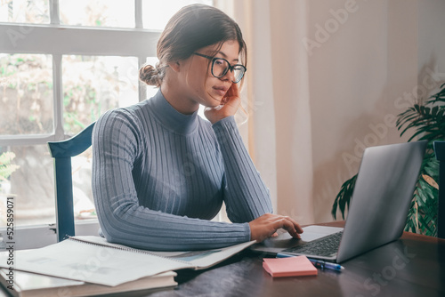 One young pretty woman studying and doing homework at home on the table. Female teenager using laptop or computer surfing the net indoor. photo