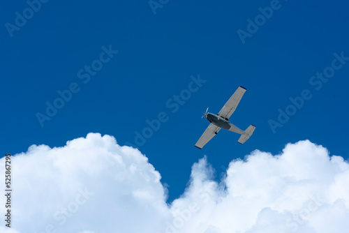 Small plane flying against blue sky and white sunlit clouds in Mexico