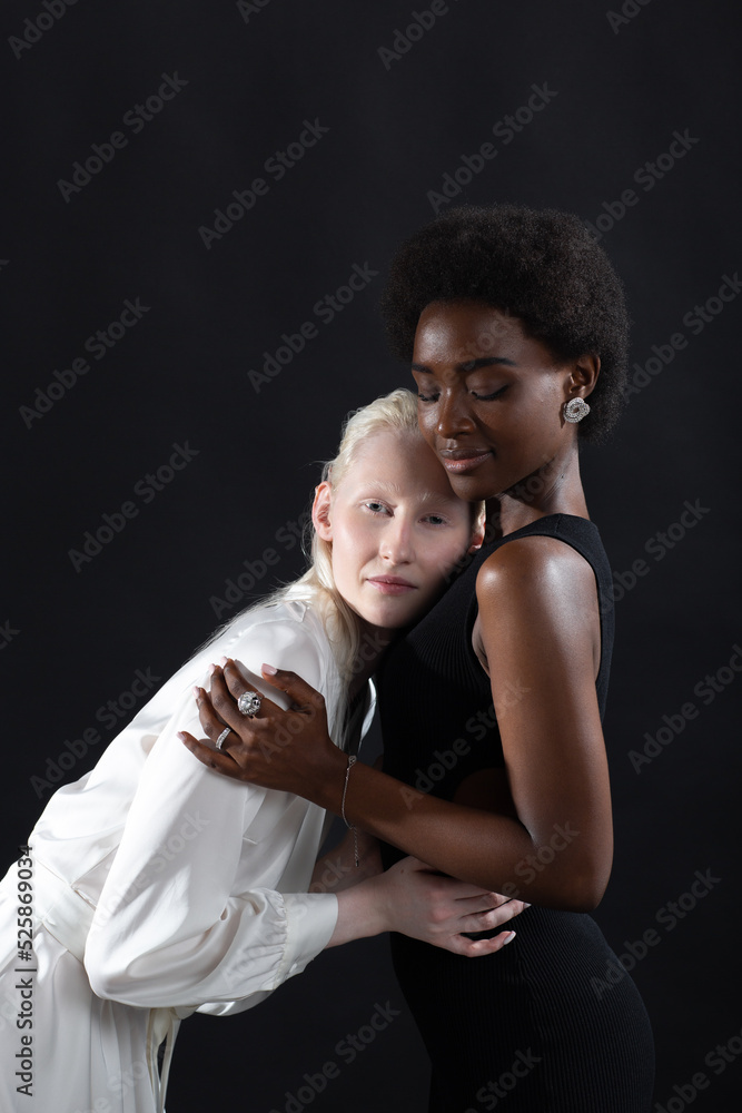 Caucasian albino girl and african american young woman hugging on black background. Women friendship, love and relationships concept. LGBT pride. Caucasian albino girl and african american young woman hugging on black background. Women friendship, love and relationships concept. LGBT pride.