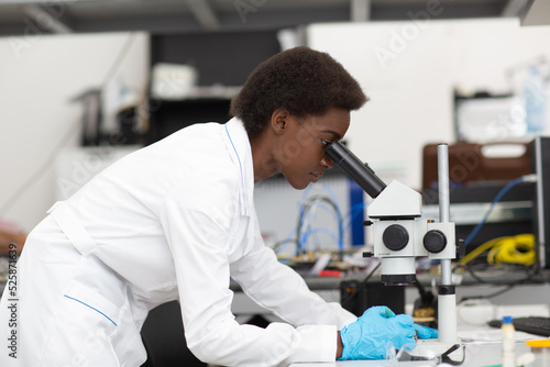 Scientist african american woman in gloves working in laboratory with electronic tech instruments and microscope. Research and development of electronic devices by color black woman.