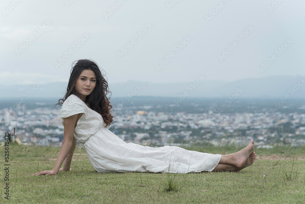 woman half sitting,half lying on grass at top mountian look at camera,sky,city and nature view background. feel relax.