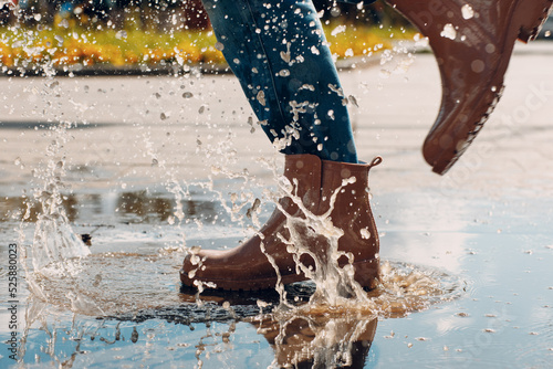 Woman wearing rain rubber boots walking running and jumping into puddle with water splash and drops in autumn rain. photo