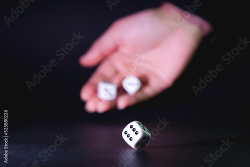 Dados blancos rodados por la mano de una mujer sobre fondo negro – enfoque selectivo.