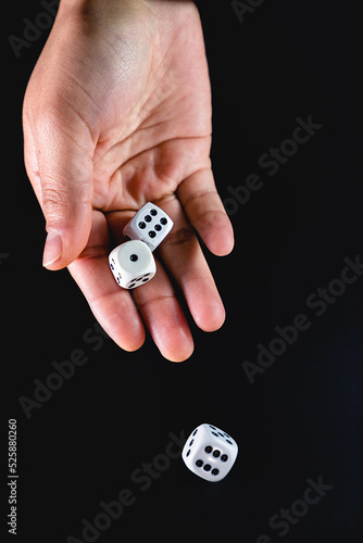 Dados blancos rodados por la mano de una mujer sobre fondo negro – enfoque selectivo.