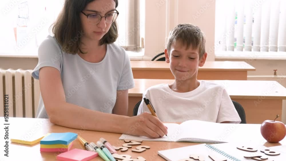A teacher teaches a boy sitting at a desk at school . A mother teaches her son to write in a notebook. The babysitter helps to complete school assignments. School and preschool education. A teacher teaches a boy sitting at a desk at school . A mother teaches her son to write in a notebook. The babysitter helps to complete school assignments. School and preschool education.