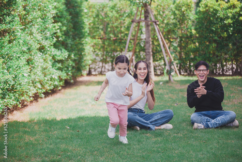 Asian Family with a child playing on a lawn, Family sitting on the grass with her happy and adorable little daughter, enjoyment relaxing recreational concept.