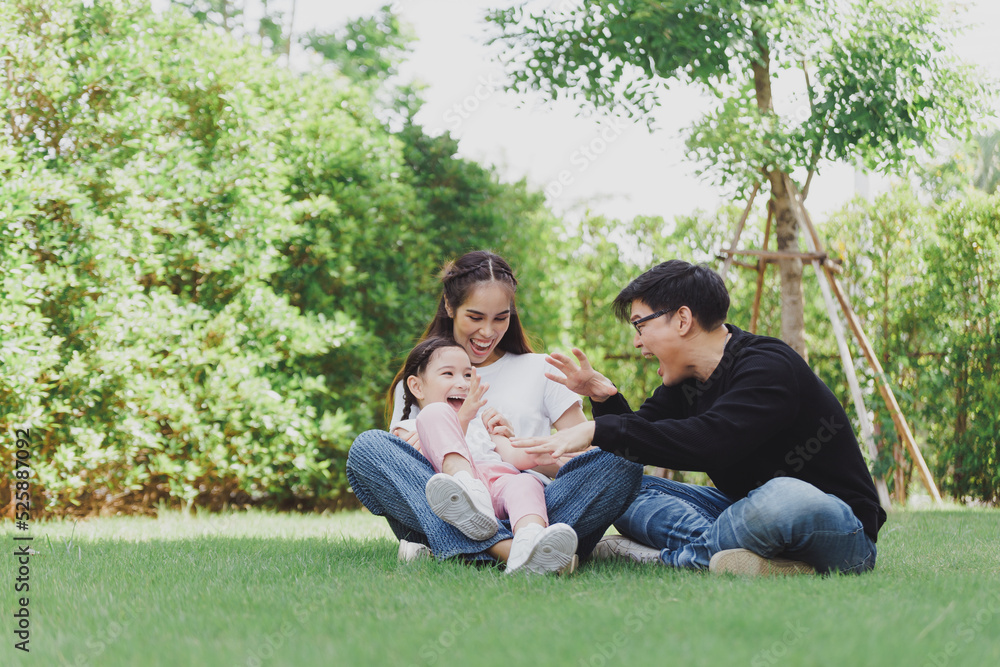 Asian Family with a child playing on a lawn, Family sitting on the grass with her happy and adorable little daughter, enjoyment relaxing recreational concept. Asian Family with a child playing on a lawn, Family sitting on the grass with her happy and adorable little daughter, enjoyment relaxing recreational concept.