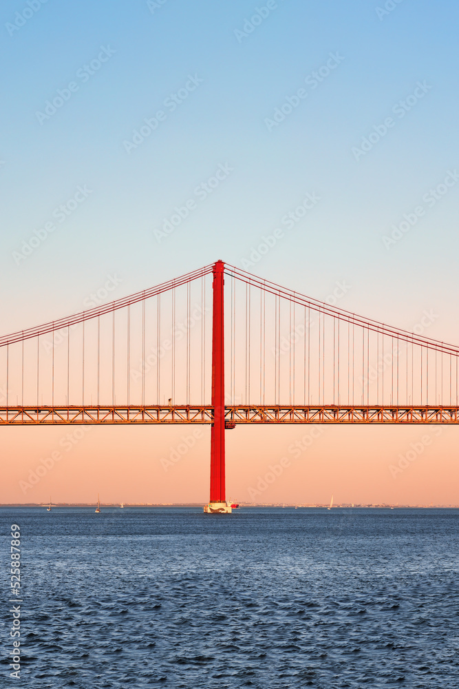 Iconic orange red suspension bridge over Tagus River in Lisbon, Portugal. 25 de Abril Bridge, 25th of April Bridge at golden hour sunset. Copy space, place your text.