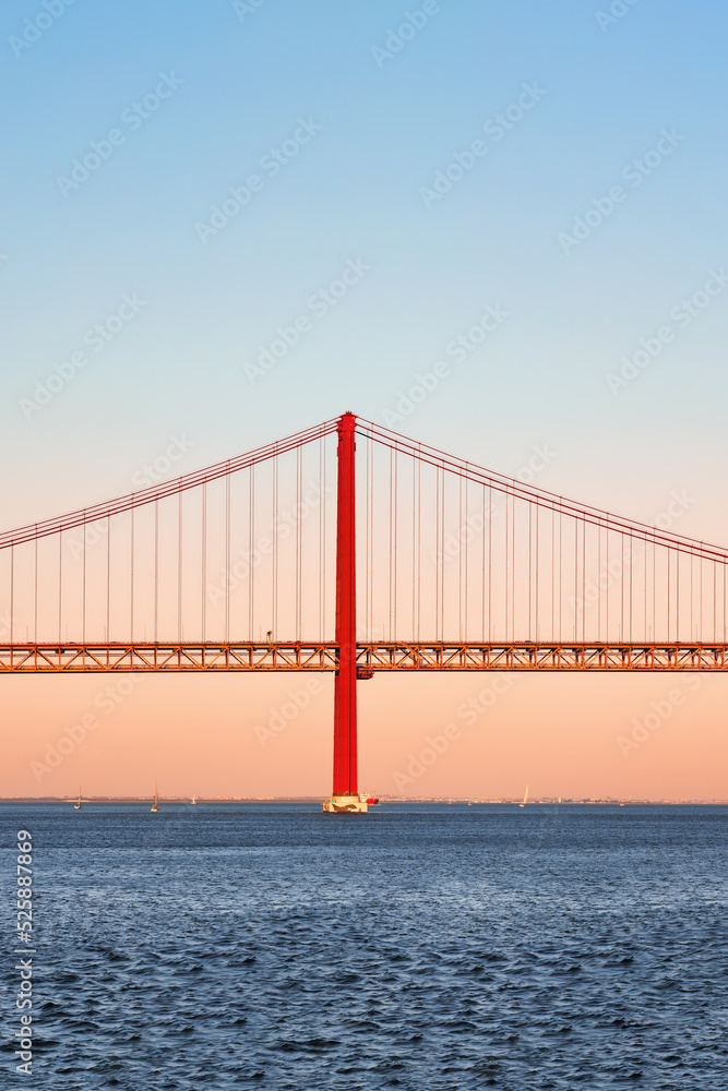 Fototapeta premium Iconic orange red suspension bridge over Tagus River in Lisbon, Portugal. 25 de Abril Bridge, 25th of April Bridge at golden hour sunset. Copy space, place your text.