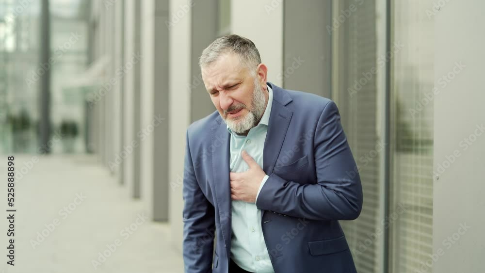 mature business man with a sudden heartache is standing on a city street near office building. Senior businessman, employee holding chest outside outdoor feeling sharp chest pain, symptom heart attack