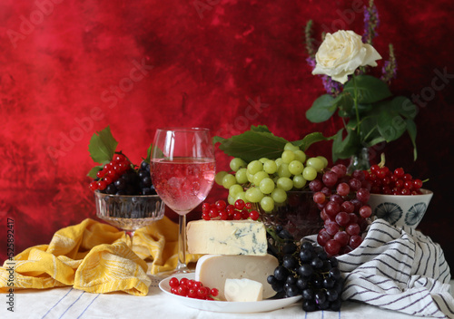 Camembert cheese, green and black grapes, glass of rose wine on a table. Colorful summer still life with seasonal fruit and berries. 