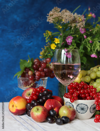 Glass of pink wine  grapes  berries and flowers on a table. Delicious summer food close up photo. Textured background with copy space.