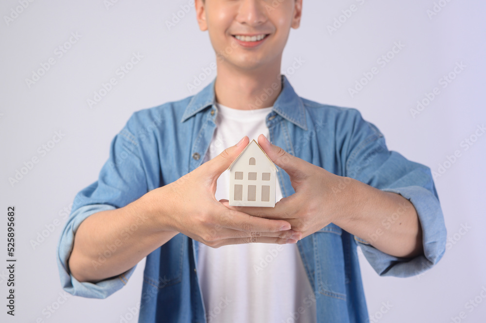 Young smiling man holding small model house over white background studio. Young smiling man holding small model house over white background studio.