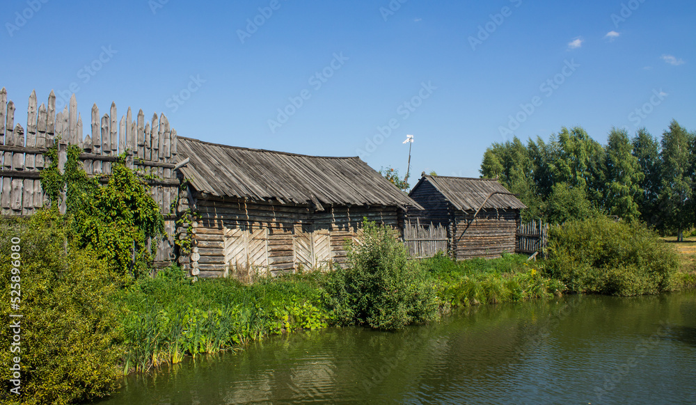 The ancient Shchurovskoye settlement in Suzdal in Russia with medieval wooden buildings among the bright green foliage of trees on the shore of a pond with a reflection on a sunny summer day The ancient Shchurovskoye settlement in Suzdal in Russia with medieval wooden buildings among the bright green foliage of trees on the shore of a pond with a reflection on a sunny summer day