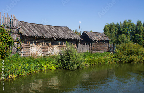 The ancient Shchurovskoye settlement in Suzdal in Russia with medieval wooden buildings among the bright green foliage of trees on the shore of a pond with a reflection on a sunny summer day
