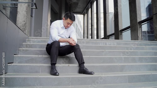 sad asian business man employee with depression worker sitting on stairs on city street near office building. outside. jobless fired businessman Lay off. Dissmissal manager Disappointed crisis problem photo