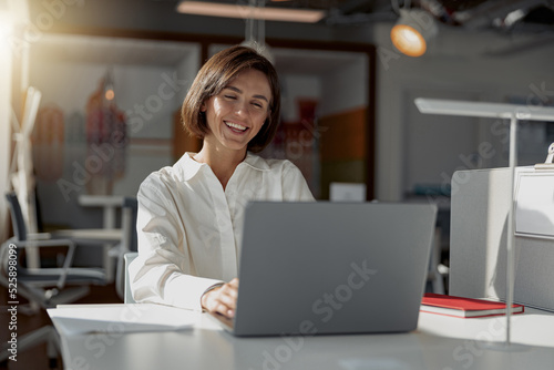 Smiling european business woman working laptop while sitting in cozy cafe. Blurred background © Yaroslav Astakhov