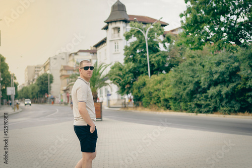 Varna, Bulgaria - 15.08.22 - Young stylish man wearing t-shirt with beard in glasses, standing on the street on city background. Street photo