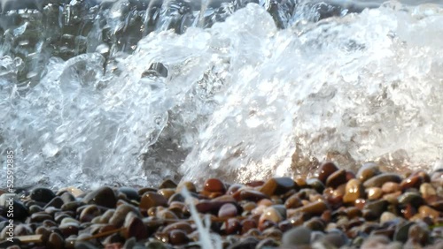 Beach waves splash over smooth colorful stones Close Up LOOP