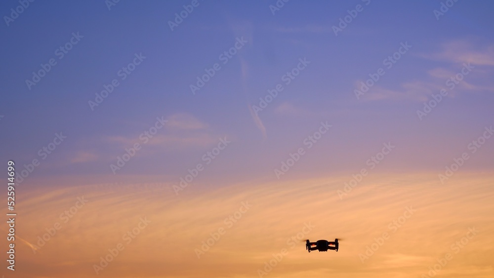 The drone takes off into the sunset sky over an unrecognizable place. A beautiful sky filled with sunset colors in which a drone flies with blinking lights. Four propellers lift the drone into the air