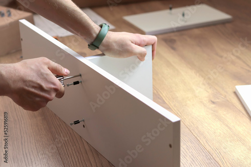 Foto The furniture assembler tightens the cam bolt fixing into the furniture made of particle board with a hex wrench, flat pack furniture assembly