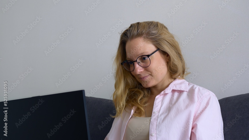A beautiful young female student puts on glasses to work on a laptop keyboard. The blonde is studying remotely via the Internet using a computer. Study at the university from home from any country. A beautiful young female student puts on glasses to work on a laptop keyboard. The blonde is studying remotely via the Internet using a computer. Study at the university from home from any country.