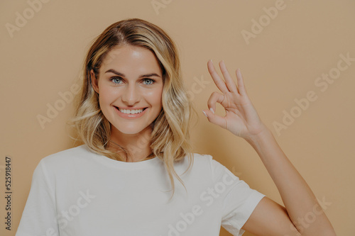 Positive cute blonde young woman in white tshirt shows OK sign with one hand