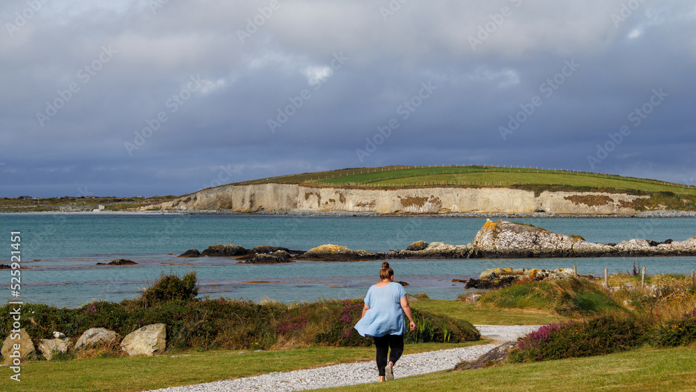 women walking down the path on the coast showing the cliffs and green grass.