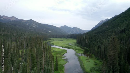 Flying over a forest of pine trees in a mountain valley with a river flowing through a shallow lake in Okanogan-Wenatchee National Forest.