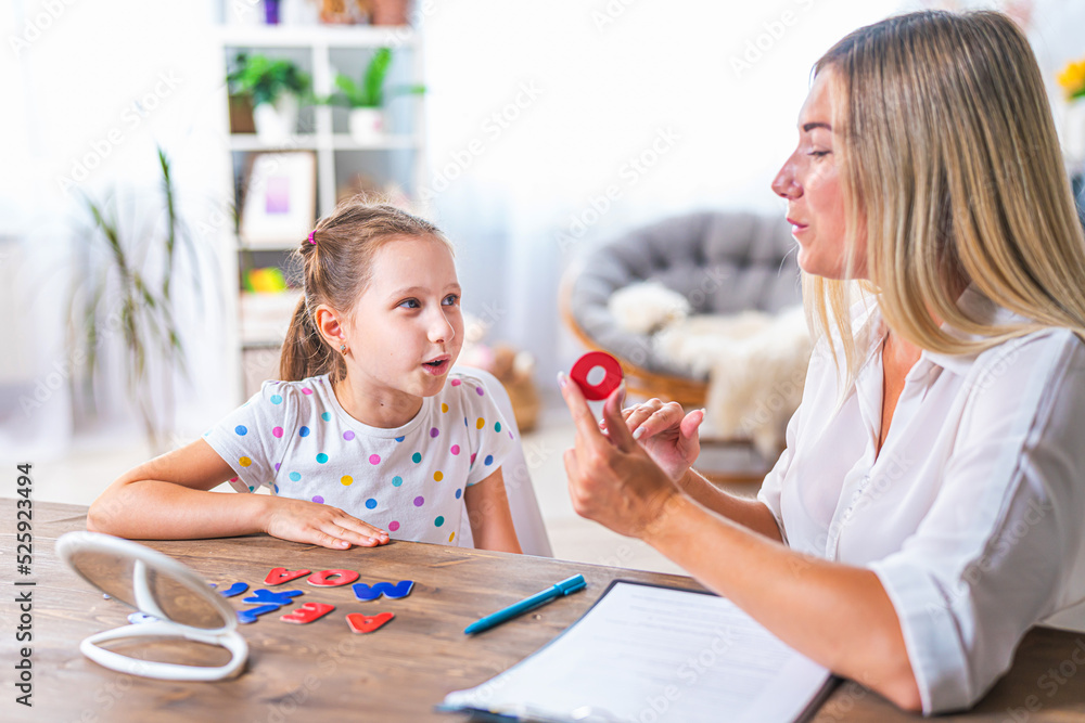 Doctor and small patient train articulation, work on problems and obstacles child with dyslexia. little girl together with speech therapist is sitting at desk indoors, playing game, studying sounds - obrazy, fototapety, plakaty 