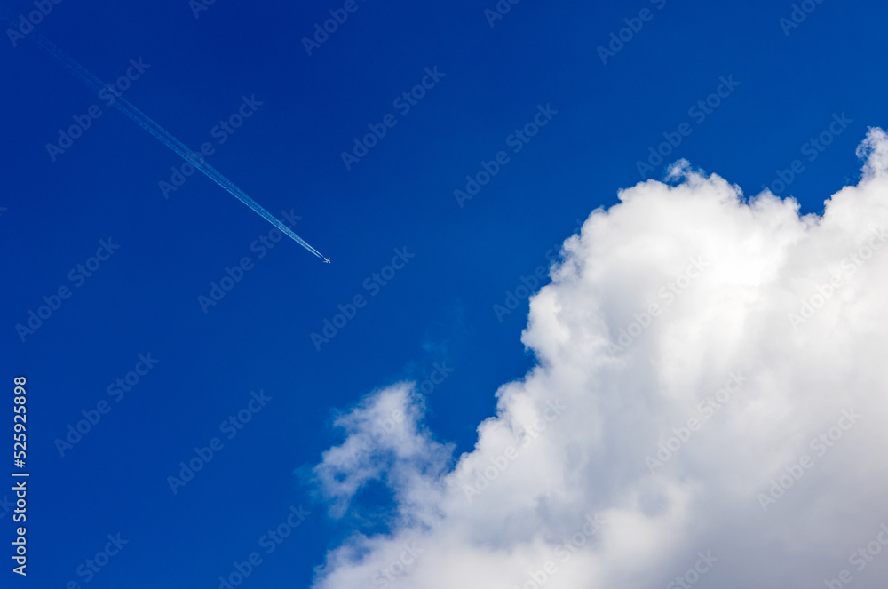 A commercial airliner with trailing contrails flies into large cloud (cumulus) on a summer day with blue sky. A commercial airliner with trailing contrails flies into large cloud (cumulus) on a summer day with blue sky.