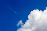 A commercial airliner with trailing contrails flies into large cloud (cumulus) on a summer day with blue sky. 