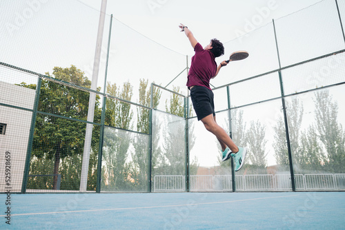 A young male paddle tennis player jumping to hit the ball in a match.
