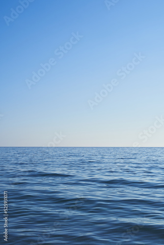 Dark blue water from the sea with blue sky. Light comes from the right. Vertical format, also suitable as a poster or background. Free space for text or objects.