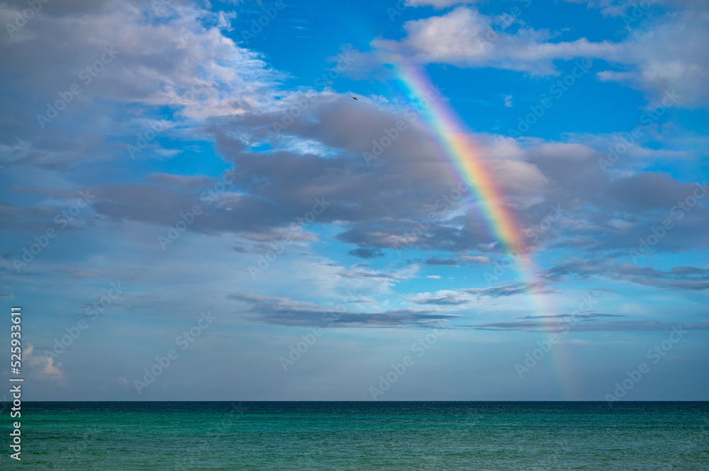 Tropical rainbow over a teal turquoise clear ocean with blue skies and partly cloudy skies