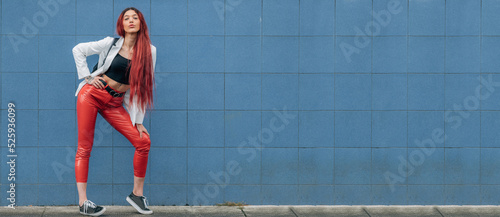 redhead funky urban hipster girl posing on the street isolated on blue wall background