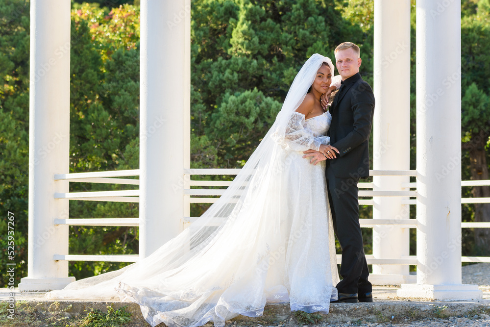 Fototapeta premium Portrait of a mixed race newlyweds in front of a gazebo with round columns