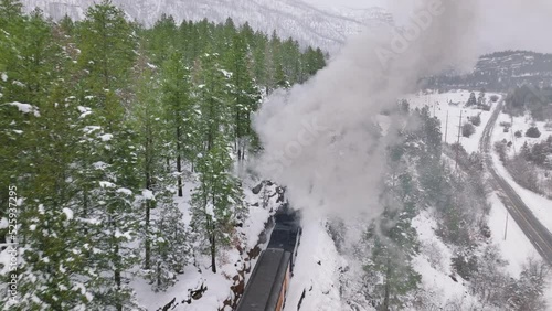 Aerial old steam locomotive, engine rides on railroad releases thick clouds of steam from pipe. Winter snowy nature. Historical American railway in Colorado mountains. Drone flying through smoke