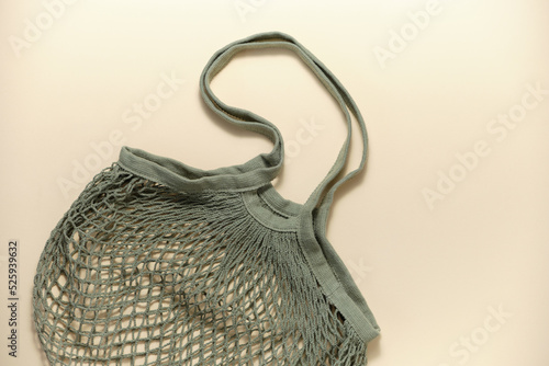 Green mesh shopping bag for groceries on a beige background. The concept of minimizing consumption, zero waste, reducing the amount of non-degradable waste.