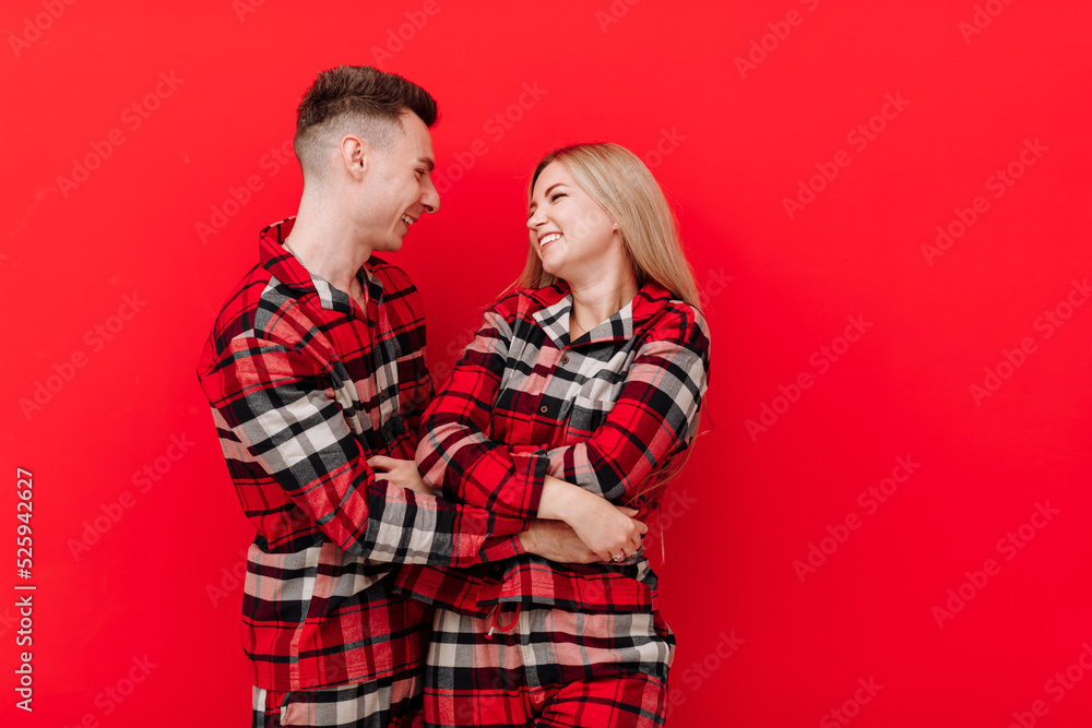 Happy Saint Valentine's Day. Smiling young couple in the same pyjamas having fun on red background. Man and woman in love are enjoying spending time together while celebrating. Happy Saint Valentine's Day. Smiling young couple in the same pyjamas having fun on red background. Man and woman in love are enjoying spending time together while celebrating.