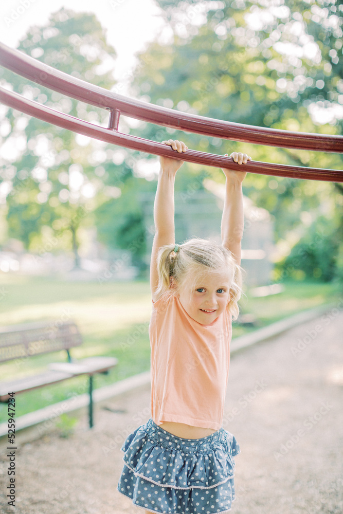 Blonde 4 year old in pigtails hangs from playground equipment. Blonde 4 year old in pigtails hangs from playground equipment.