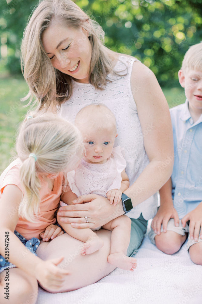 Toddler girl kisses baby sister on cheek while sitting with family. Toddler girl kisses baby sister on cheek while sitting with family.