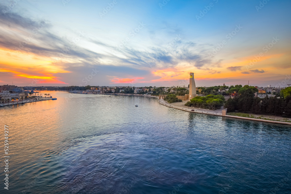 The Italian Sailor Monument can be seen along with the seaside port city of Brindisi, Italy, at sunset. Viewed from a cruise ship at sea in the Puglia region of Italy.